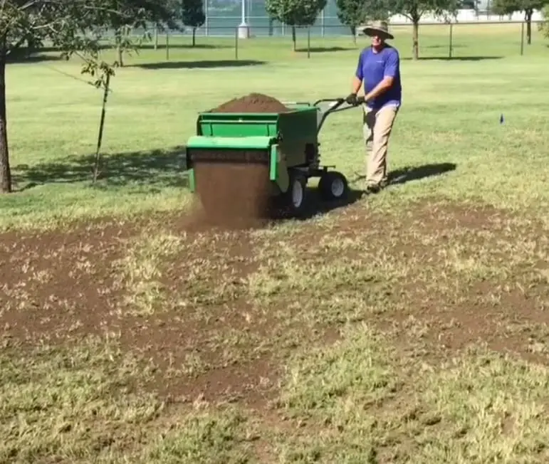 A man using a lawn seed spreader to spread grass.