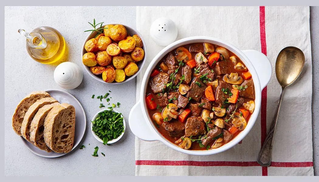 A bowl of stew and some other food on the table.