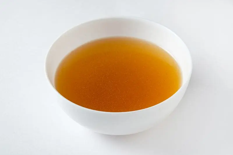 A bowl of broth is sitting on the table.